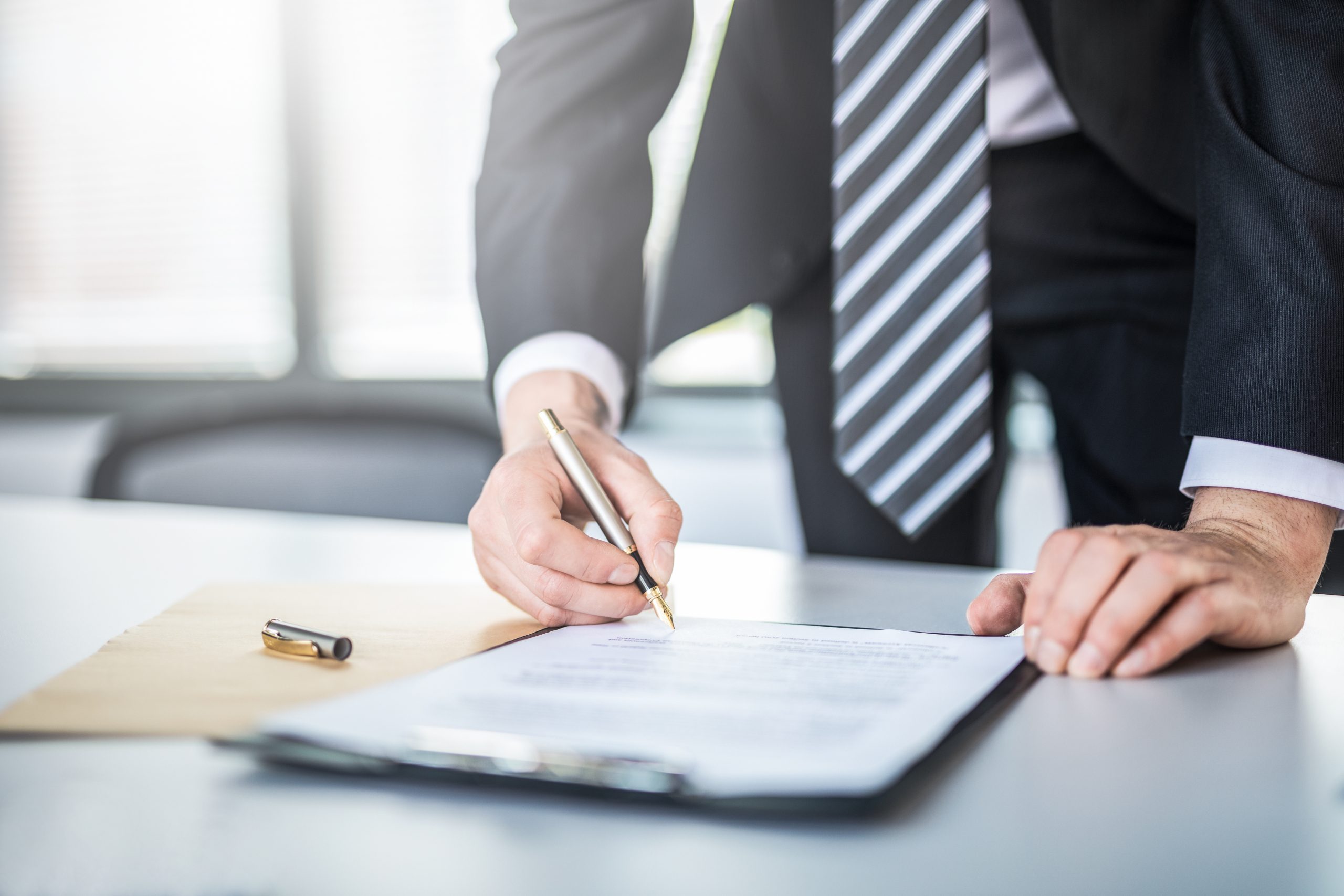 Business man signing contract document on office desk, making a deal.