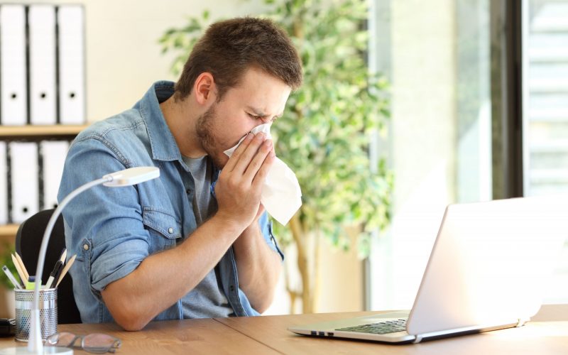 Side view of an ill entrepreneur sneezing in a wipe at office near a window