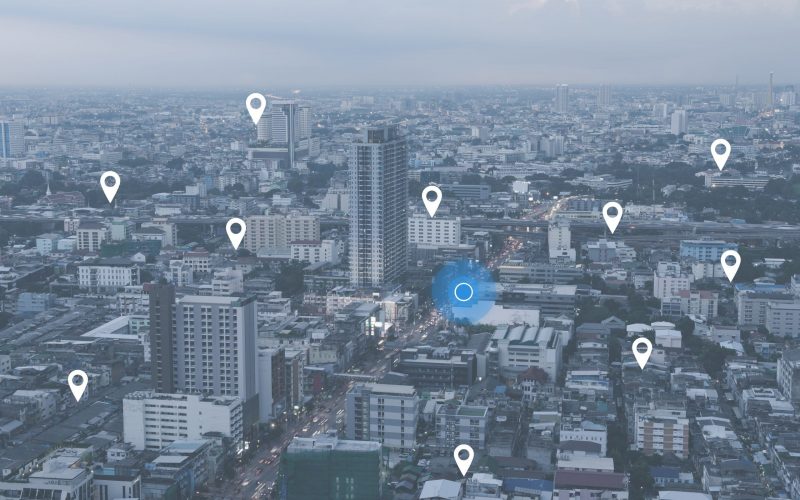 Searching location on map and pin above blue tone city scape and network connection, internet of things, satellite navigation system concept