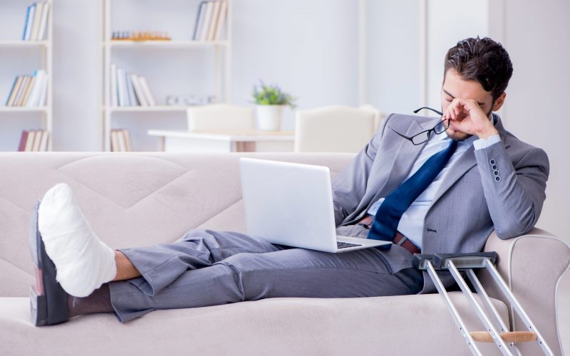 Businessman with crutches and broken leg at home working