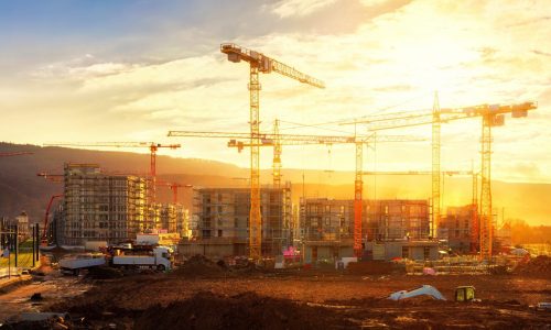 Large construction site including several cranes working on a building complex, illumined by warm gold sunlight