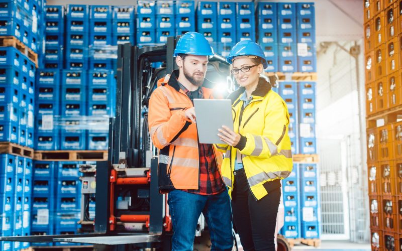 Workers in warehouse checking data on tablet computer with forklift in the background