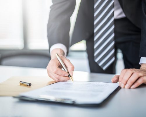 Business man signing contract document on office desk, making a deal.