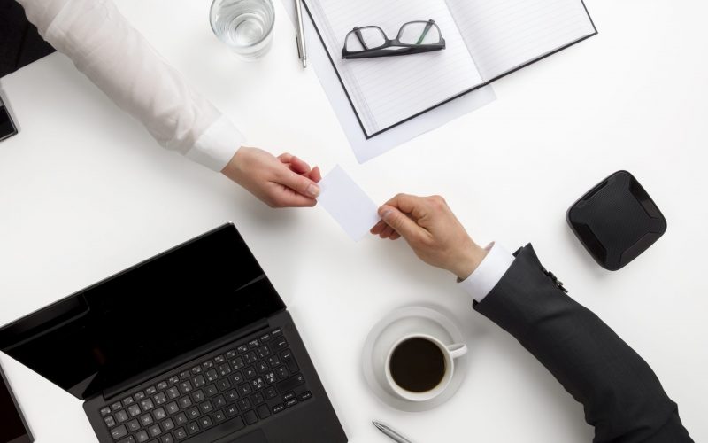 Overhead view of business colleagues exchanging visiting card at white office desk